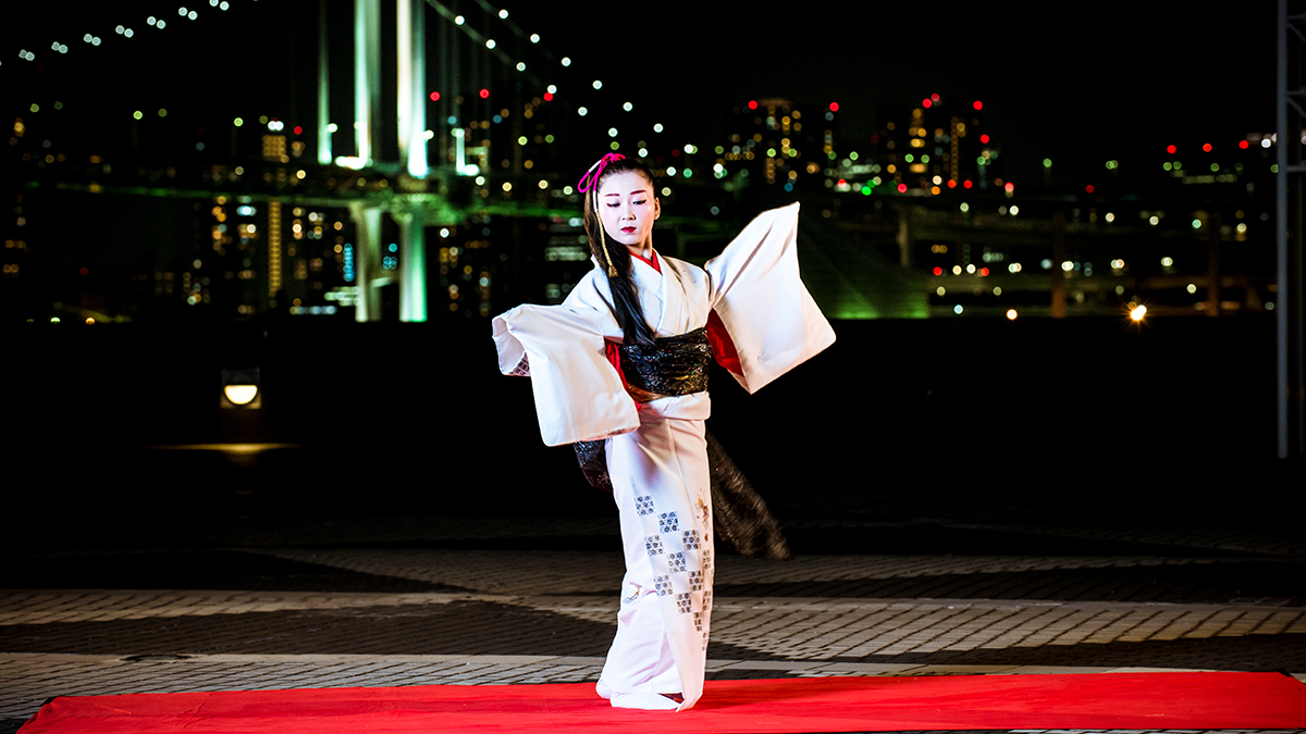 A DEN Tokyo dancer performing Nihon Buyo against the Tokyo Bay skyline at night