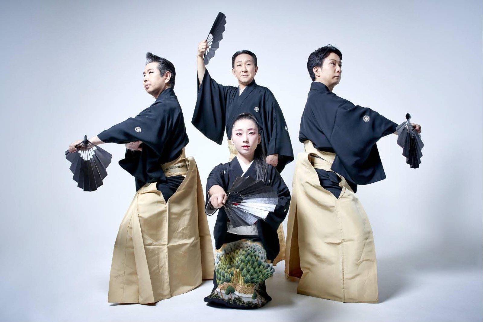 Four DEN Tokyo dancers in black montsuki and gold hakama, poised with fans